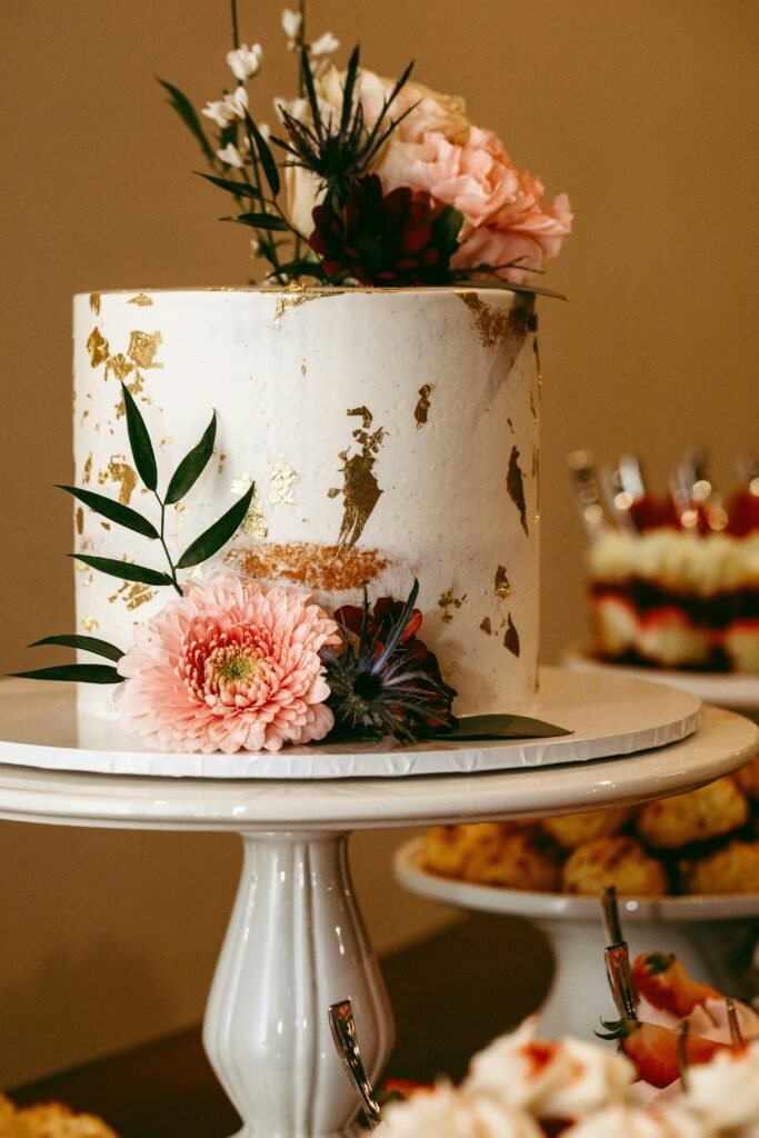 A beautifully decorated wedding cake with fresh flowers and gold accents on a cake stand.