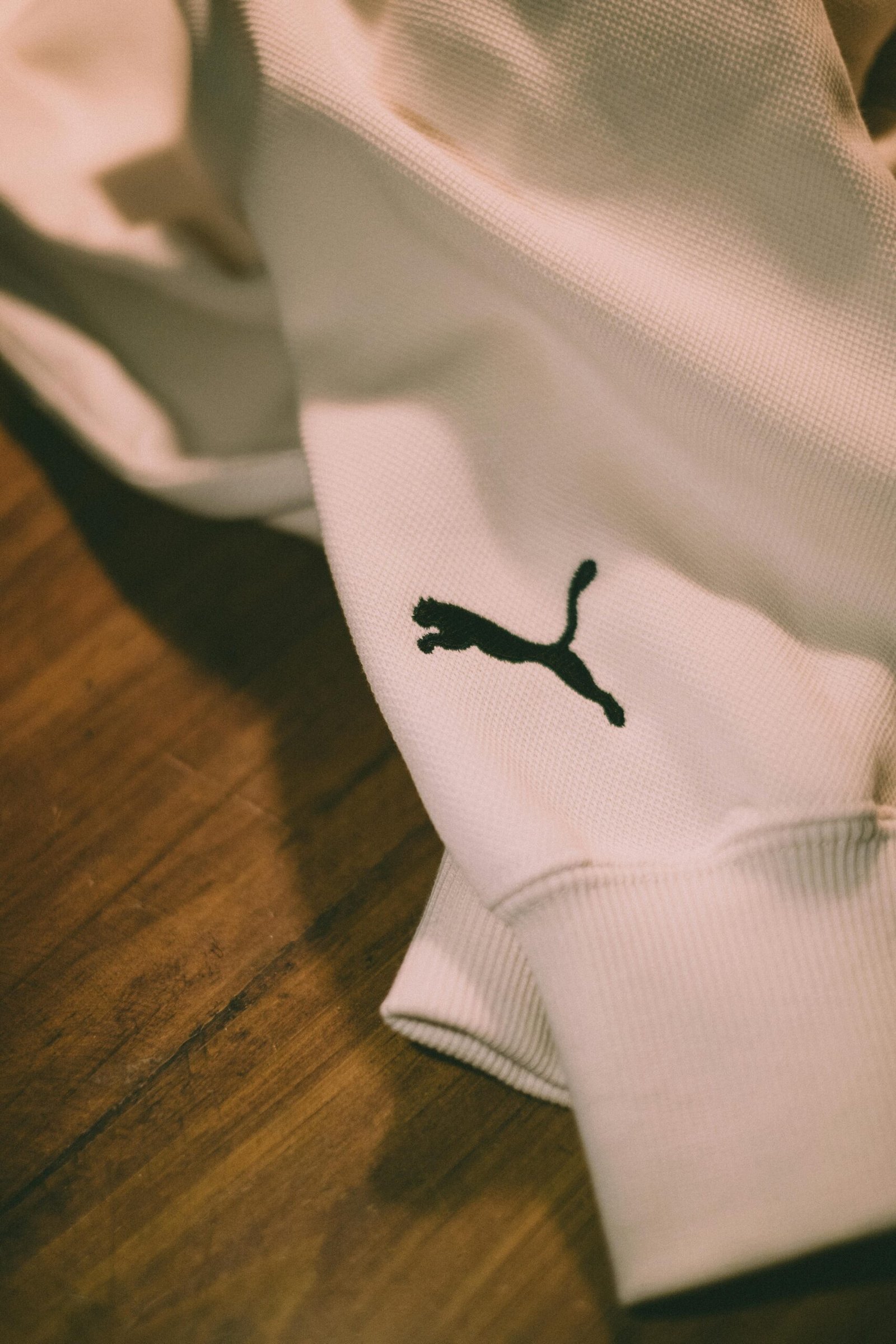 Artistic close-up of a white sweater featuring a black logo on wood background.
